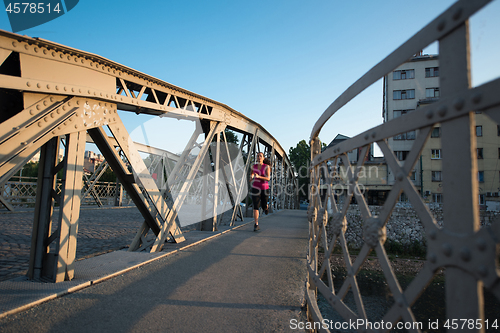 Image of woman jogging across the bridge at sunny morning