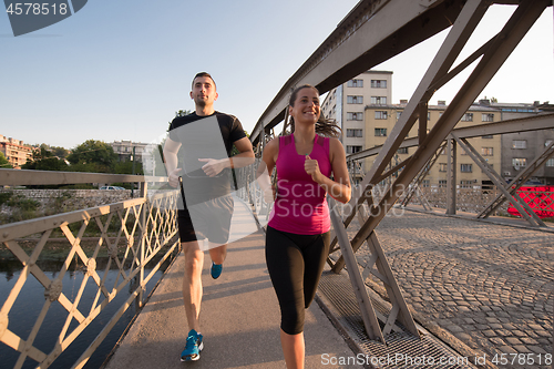 Image of young couple jogging across the bridge in the city