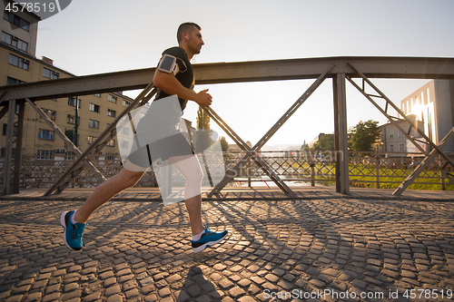 Image of man jogging across the bridge at sunny morning