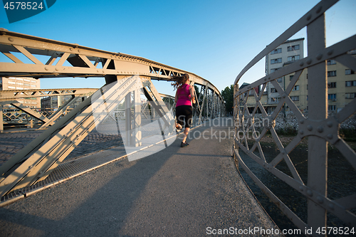 Image of woman jogging across the bridge at sunny morning