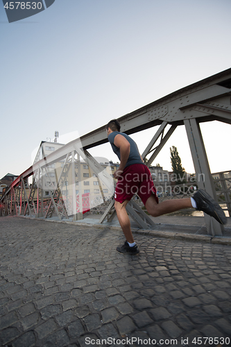 Image of man jogging across the bridge at sunny morning