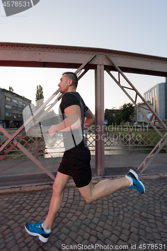 Image of man jogging across the bridge at sunny morning