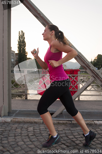 Image of woman jogging across the bridge at sunny morning