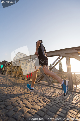 Image of man jogging across the bridge at sunny morning