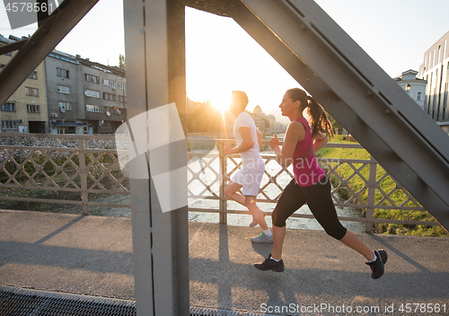 Image of young couple jogging across the bridge in the city