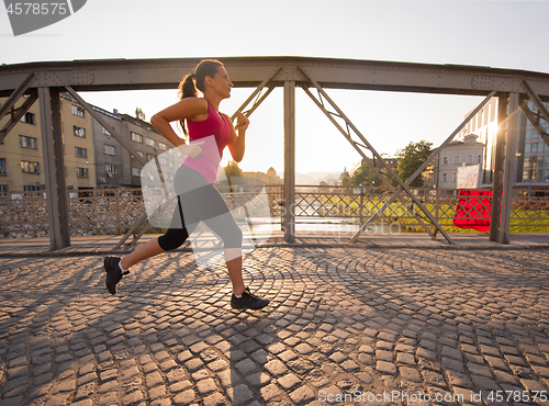 Image of woman jogging across the bridge at sunny morning