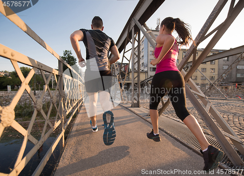 Image of young couple jogging across the bridge in the city