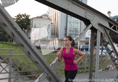 Image of woman jogging across the bridge at sunny morning