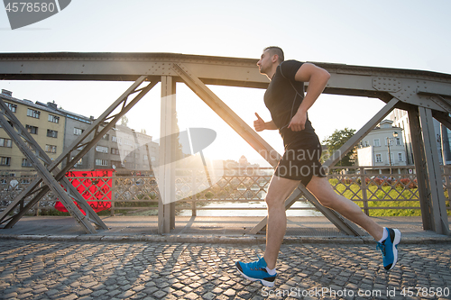 Image of man jogging across the bridge at sunny morning