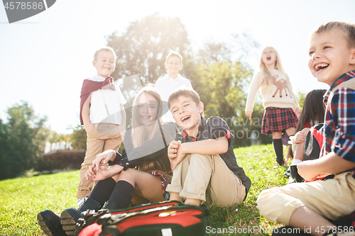 Image of A group of children of school and preschool age are sitting on the green grass in the park.