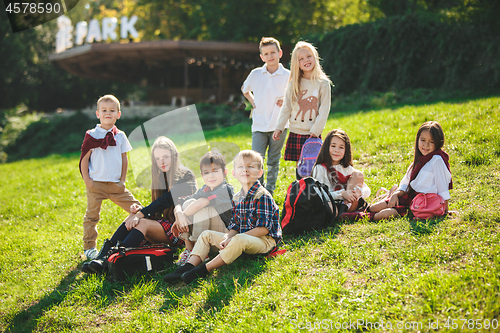 Image of A group of children of school and preschool age are sitting on the green grass in the park.