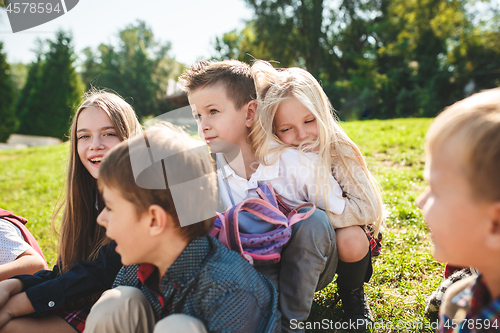 Image of A group of children of school and preschool age are sitting on the green grass in the park.