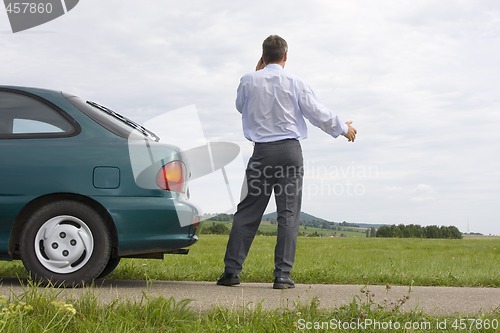 Image of Businessman talking on cell phone beside his car