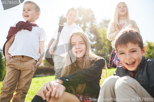 Image of A group of children of school and preschool age are sitting on the green grass in the park.