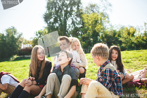 Image of A group of children of school and preschool age are sitting on the green grass in the park.