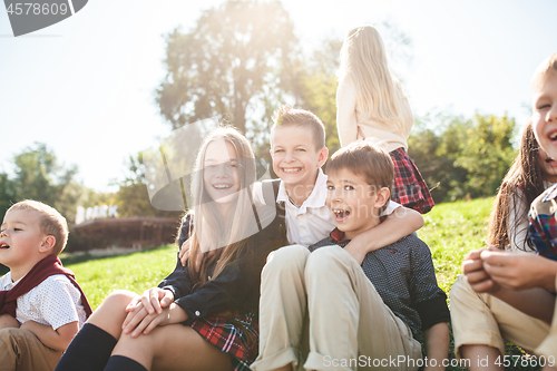 Image of A group of children of school and preschool age are sitting on the green grass in the park.