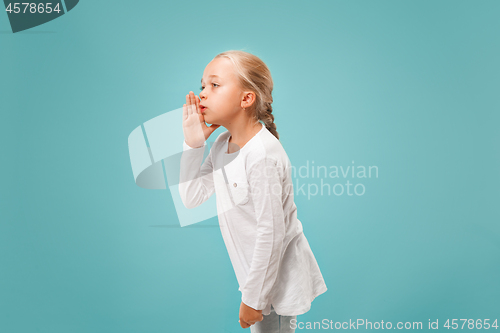 Image of The young teen girl whispering a secret behind her hand over blue background