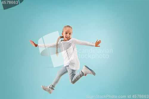Image of Adorable small child at blue studio. The girl is jumping and smiling.