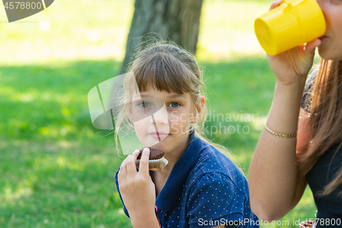 Image of Girl eating a cupcake on a picnic, next to a girl drinking tea