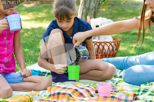 Image of At a picnic, a girl pours tea in glasses for children