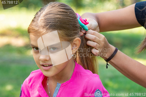 Image of A teenager girl is tied a bow on long hair, on a picnic, close-up