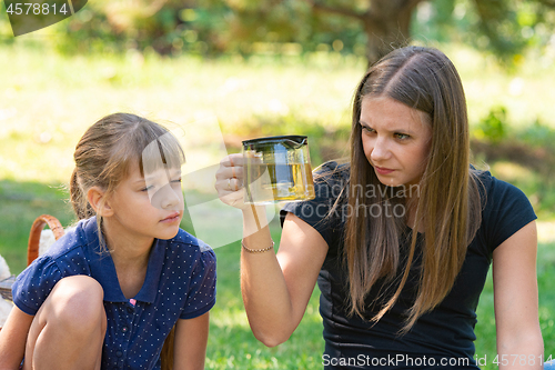 Image of Girl and girl with interest look at a teapot at a picnic