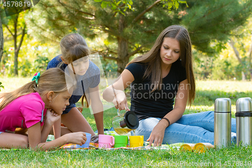 Image of Family on a picnic, girl pours tea in glasses, children watch