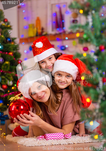 Image of Mom and two daughters lie on the floor of a Christmas tree in the New Year\'s interior