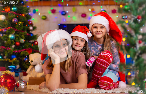 Image of Mom and two daughters lie on the floor of a Christmas tree
