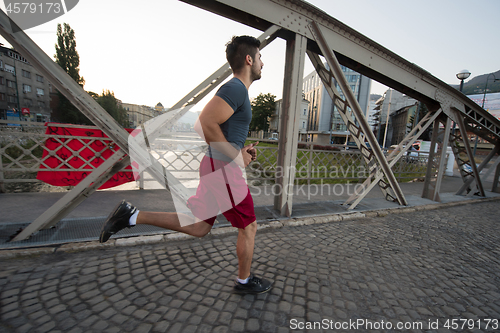 Image of man jogging across the bridge at sunny morning