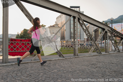 Image of woman jogging across the bridge at sunny morning
