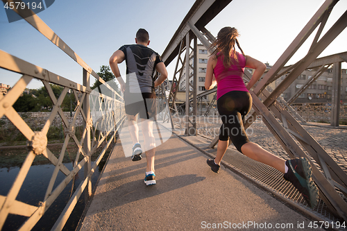 Image of young couple jogging across the bridge in the city