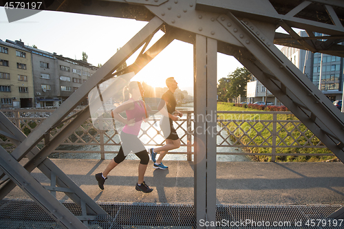 Image of young couple jogging across the bridge in the city