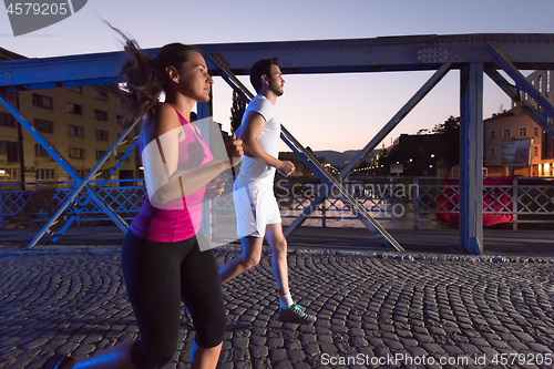Image of couple jogging across the bridge in the city