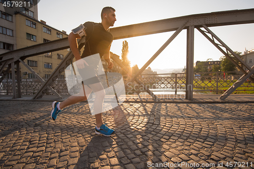 Image of man jogging across the bridge at sunny morning