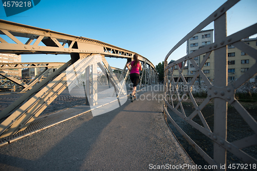 Image of woman jogging across the bridge at sunny morning