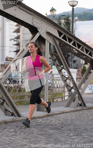 Image of woman jogging across the bridge at sunny morning