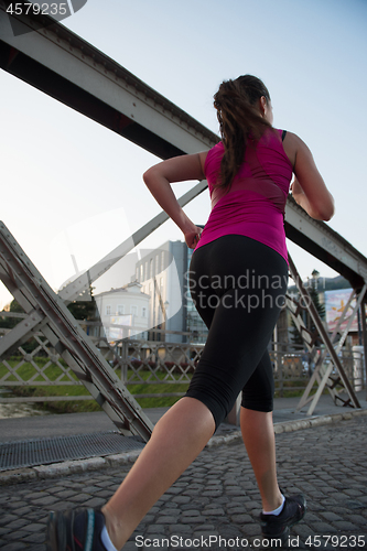 Image of woman jogging across the bridge at sunny morning