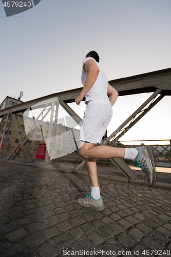 Image of man jogging across the bridge at sunny morning