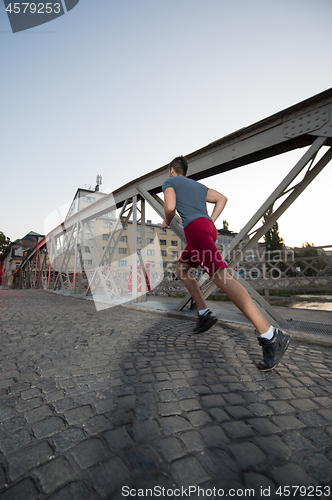 Image of man jogging across the bridge at sunny morning