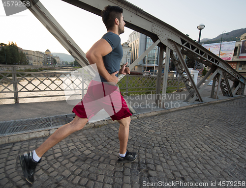 Image of man jogging across the bridge at sunny morning