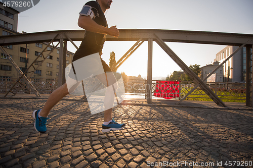 Image of man jogging across the bridge at sunny morning