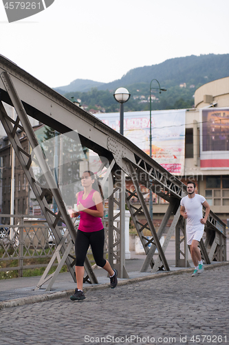 Image of young couple jogging across the bridge in the city