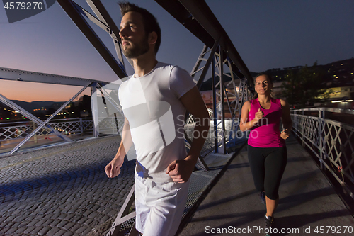 Image of couple jogging across the bridge in the city