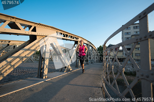 Image of woman jogging across the bridge at sunny morning