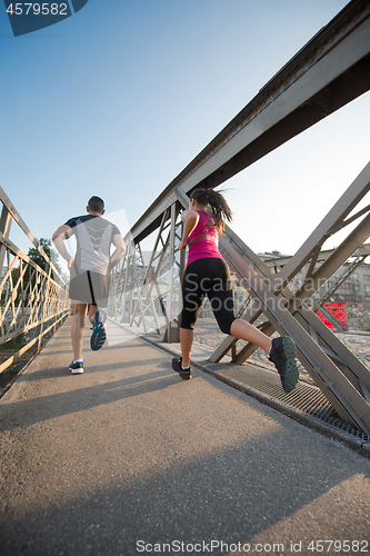 Image of young couple jogging across the bridge in the city