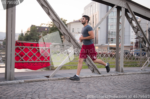 Image of man jogging across the bridge at sunny morning