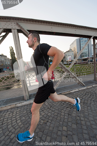 Image of man jogging across the bridge at sunny morning