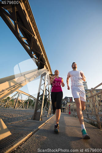 Image of young couple jogging across the bridge in the city