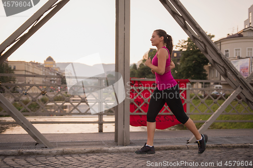 Image of woman jogging across the bridge at sunny morning